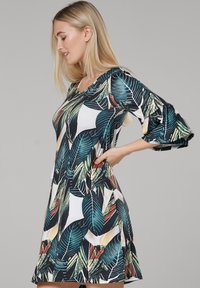 Kurzärmliges Kleid mit einem lebendigen grünen Blattdruck auf dunklem Hintergrund, gefertigt aus weichem Stoff mit weiter Silhouette und seitlichen Taschen.