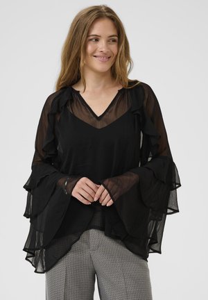 Black sheer blouse with V-neck and layered ruffled sleeves, featuring a flowy design. Paired with patterned gray trousers.