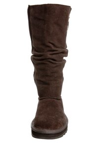 Bota de ante marrón hasta la rodilla con un diseño arrugado, punta redondeada, superficie texturizada y costuras contrastantes alrededor de la suela.