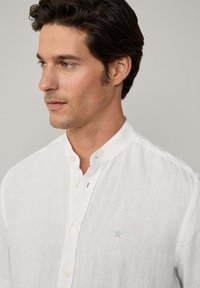 Witte linnen blouse met een bandkraag en knoopsluiting, voorzien van een klein lichtblauw embleem op de linkerborst. Zachte en gestructureerde stof.