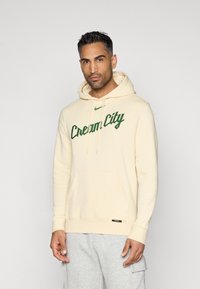 Hoodie v kremni barvi z zelenim napisom "Cream City". Ima sprednji žep, kapuco s vezalko in rebraste manšete. Mehka tekstura tkanine.
