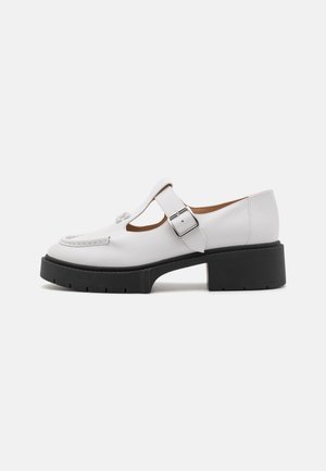 Zapato de cuero blanco con diseño de barra en T, hebilla plateada y una suela de plataforma negra gruesa. Presenta acentos de costura a lo largo de la parte superior.