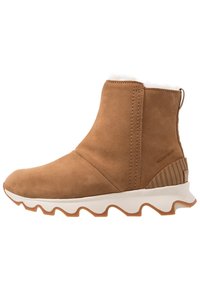 Wodoodporny, brązowy zamszowy botek za kostkę z teksturowanym gumowym obcasem i białą podeszwą w zygzak. Wyściełany miękkim materiałem przy mankiecie.