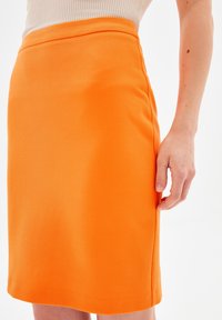 Gonna a matita arancione in tessuto strutturato, con design aderente, orlo al ginocchio e dettagli sulla cucitura laterale.