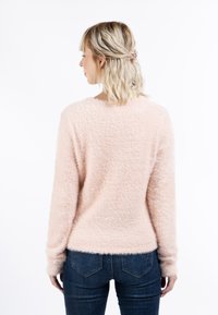 Lichtroze, fluffy trui met lange mouwen en een ronde halslijn. Heeft een zachte textuur en valt tot de heup, gecombineerd met donkere spijkerbroek.