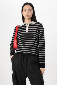 Polo a maniche lunghe nera con strisce bianche e beige, caratterizzato da un colletto beige e una chiusura con tre bottoni, indossato con pantaloni cargo neri.