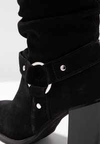 Mustat mokka nilkkurit, joissa on leveä hihna, jossa on hopeinen pyöreä korostus, hopeisia niittejä ja paksu korko vakaata tukea varten.