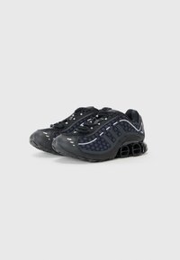 Black athletic shoes with mesh panels and a textured surface. Features elastic laces, reflective accents, and a distinctive cushioned sole.
