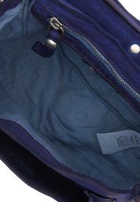 Vista interna di una borsa vuota in suede blu con una tasca con zip e un'etichetta di cura del tessuto all'interno.