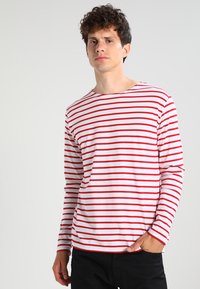 Camicia a maniche lunghe in cotone bianco con righe orizzontali rosse, caratterizzata da un collo rotondo e una vestibilità rilassata. Nessun accento o motivo particolare.