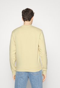 Sudadera beige con cuello redondo, mangas largas y puños de canalé, combinada con jeans de corte relajado en azul claro. Textura de tela suave.