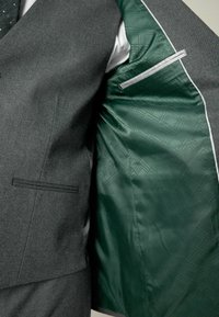 Sacou gri cu un exterior texturat, buzunar pe piept, și căptușeală cu model verde. Include un buzunar cu fermoar și detalii cu piping alb.
