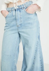 Pantalones de mezclilla anchos de color azul claro con cintura alta, bolsillos delanteros y detalles de costura visibles. Textura suave y corte relajado.