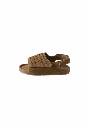 Sandal in suede marrone con punta aperta, caratterizzata da una fascia intrecciata sul dorso del piede e una fascetta posteriore per il supporto. Suola piatta, design minimale.