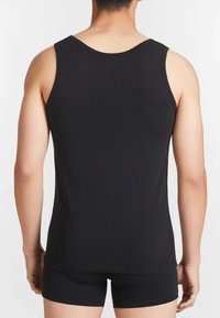Top in cotone nero senza maniche con scollo rotondo, caratterizzato da un design aderente e spalline larghe. Indossato con pantaloni corti neri abbinati.