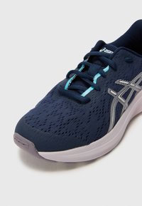 Chaussure de sport bleu foncé avec une tige texturée, un design léger, des accents argentés réfléchissants et une semelle blanche douce. Lacets de couleur bleue assortie.