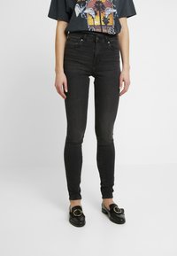 Svarta skinny jeans med en slät textur och hög midja. I kombination med svarta loafers med en rund detalj.