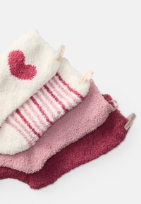 Fyra par fluffiga strumpor utställda. Vita med rosa hjärtan, rosa randiga, enfärgat ljusrosa och mörkrosa, alla med texturerade ytor och etiketter.