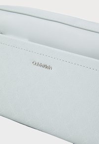 Portafoglio Calvin Klein azzurro chiaro con un Intricato motivo in rilievo, caratterizzato da un logo argentato e dettagli di cucitura sottili. Texture liscia.