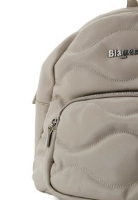Zaino grigio chiaro con una superficie texturizzata a motivo ondulato. Presenta una tasca frontale con zip e un accento del logo argento nella parte superiore.