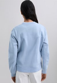 Sudadera azul claro con textura acanalada, cuello redondo y mangas largas. Presenta una costura horizontal en la parte posterior y puños ajustados.