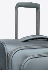 Valise en tissu gris avec une poignée télescopique à prise arrondie, accentuée par une fermeture éclair robuste et des détails de marque.