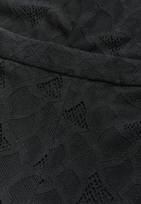 Svart texturerad tyg med ett geometriskt mönster och öppna områden, som kombinerar en slät väv med en nätliknande design.