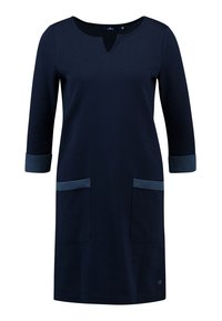 Laivastonsininen polvipituinen mekko, jossa on kolme neljäsosahihan mittaiset hihat, lovellinen pääntie ja kaksi etutaskua, joissa on tummempi reunus.