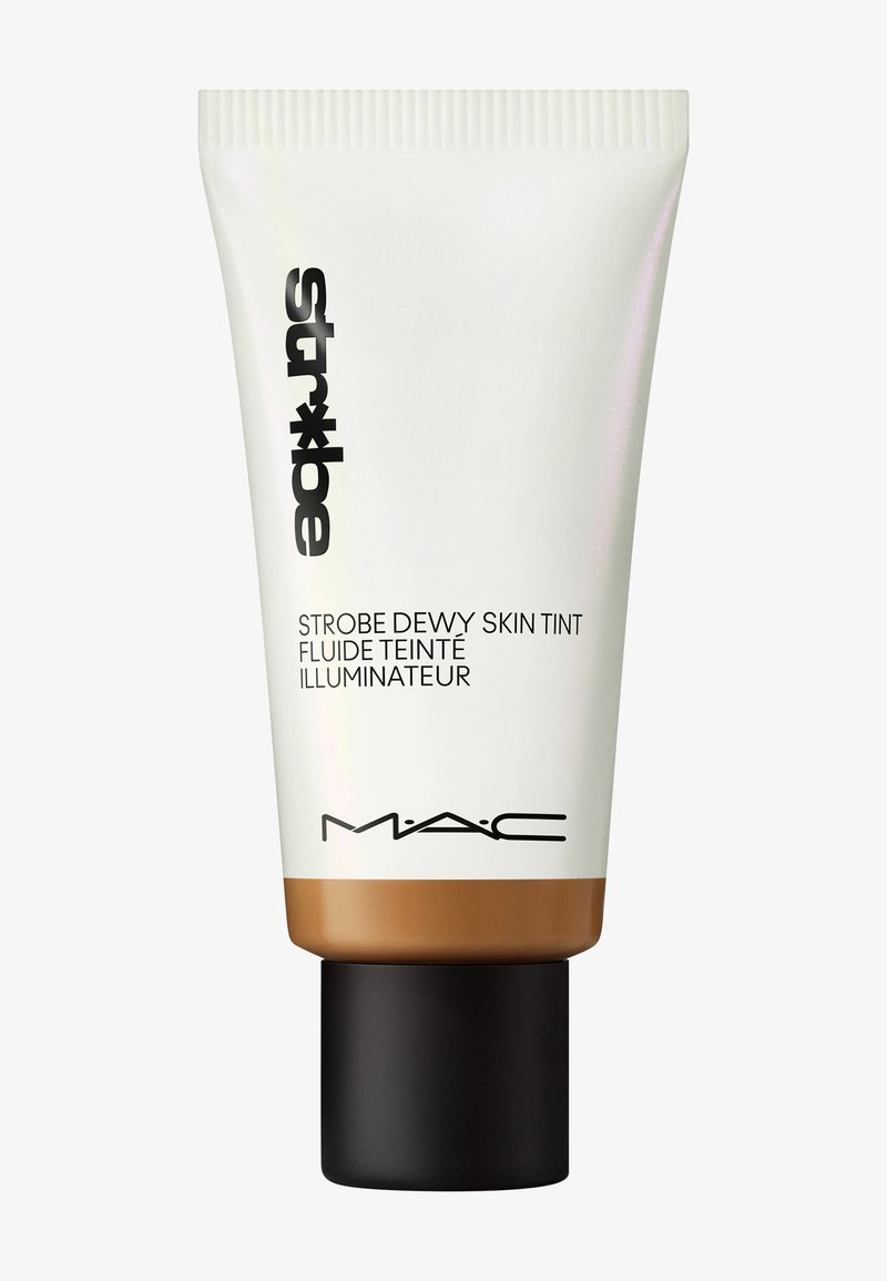 Tuba med MAC Strobe Dewy Skin Tint; vit med en bronsbas, har ett svart lock och djärv svart text på framsidan. Slät textur.