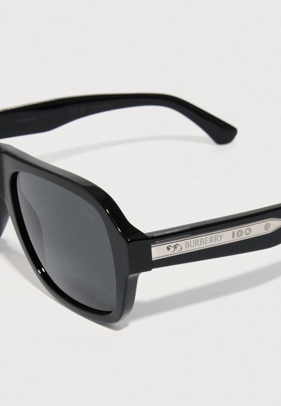Czarne okulary przeciwsłoneczne z grubą oprawką, ciemnymi soczewkami i metalicznymi ozdobami po bokach z nazwą marki "Burberry".