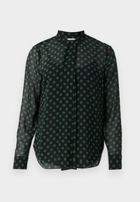 Blouse noire transparente à manches longues avec des pois verts, col montant et poignets boutonnés, présentée sur fond blanc.