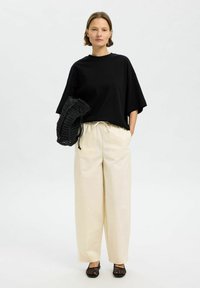 T-shirt noir surdimensionné, pantalon large crème, sac tissé noir et chaussures noires. Tissu lisse, coupe décontractée et détail de taille à cordon.