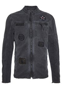 Harmaa farkkutakki, jossa vetoketju edessä, useita paikkoja ja teksturoidut saumat. Takissa on pystykoristeinen kaulus ja rintatasku.