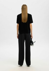 Melna īsām piedurknēm topiņš, kombinēts ar augsto vidukli melnām platām biksēm, turēts rokās ar mazu melnu somiņu. Sleek, minimālistisks dizains.