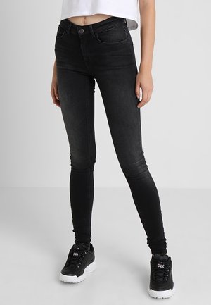 Jeans skinny negros de denim, con un diseño clásico de cinco bolsillos, cintura de altura media y un leve desgastado. Combinados con zapatillas negras.