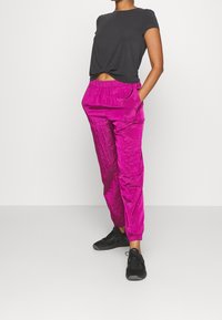 Camiseta negra de algodón ajustada con un frente anudado, combinada con pantalones jogger de textura vibrante en color rosa, que cuentan con una cintura elástica y bolsillos laterales.