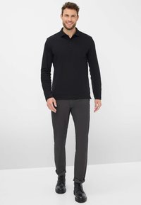 Polo à manches longues noir avec col, doté d'une poche avant. Associé à un pantalon texturé gris foncé et des bottes noires à lacets.