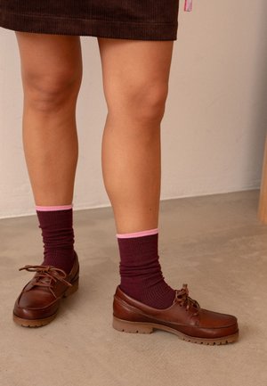 Scarpe in pelle marrone con suole in gomma, abbinate a calzini a coste color marrone bordeaux con risvolti rosa, indossati con una gonne in corduroy marrone.