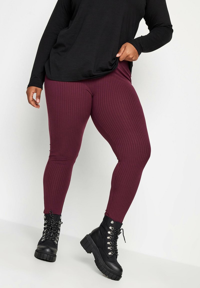 Leggings côtelés bordeaux en matière extensible, associés à des bottes de combat noires à lacets avec une semelle épaisse et des éléments en métal argenté.