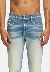 Light blue denim jeans with a distressed finish, featuring five pockets, metal button closure, and frayed edges at the pocket openings.