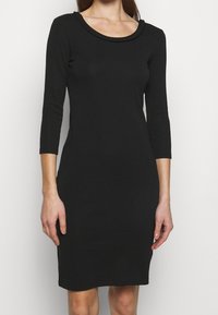 Svart klänning med lång ärm och figursydd design samt en rund, flätad halsringning. Tillverkad av mjukt tyg, den sträcker sig till mitten av låret.