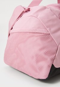 Sac de sport rose en tissu avec un panneau en maille texturée, une surface lisse et une base noire contrastante. Comprend des sangles ajustables et une fermeture éclair.