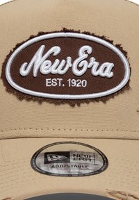 Μπεζ ρυθμιζόμενο καπέλο με καφέ κεντημένο λογότυπο, με υφασμάτινο ένθετο, στρογγυλό σχήμα και στρογγυλή ετικέτα στο γείσο.