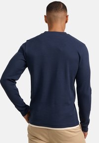 Marineblauw geribd shirt met lange mouwen, een ronde hals en nauwsluitende mouwen, met een textuurstof en een minimalistisch ontwerp.