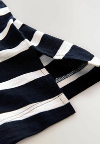 Jūras flotes un balta stripes audums ar brīvu piegriezumu. Redzama šuvju detaļa un atvērts piedurknes dizains. Mīksta tekstūra, viegla materiāla.