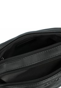 Interno di una borsa in pelle nera con molteplici scomparti con cerniera e una texture liscia. Presenta una cucitura intricata lungo le cerniere.
