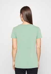 Lyhytnenkkinen vihreä t-paita, joka on valmistettu puuvillasta. Paidassa on pyöreä kaula-aukko ja sileä pinta. Takakuvassa näkyy yksinkertainen malli ilman koristeluita.