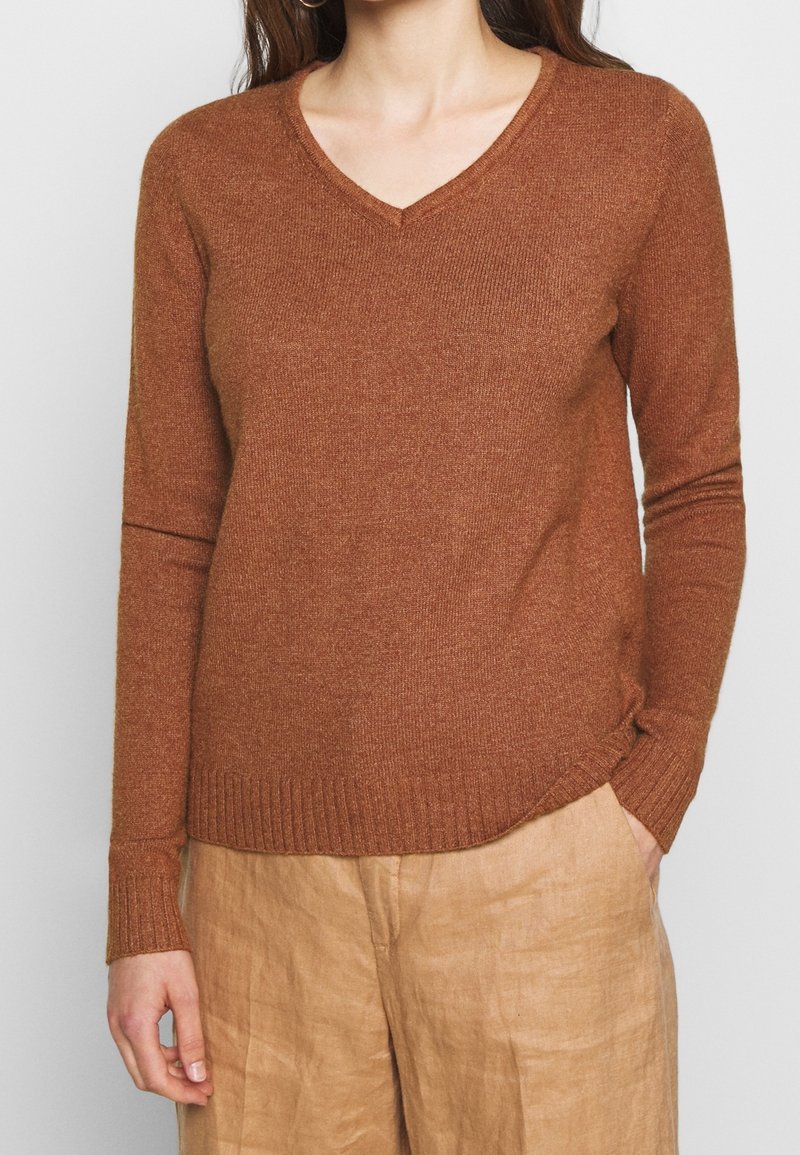 Brun, långärmad tröja i ett strukturerat material. Har en V-ringning och ribbad nederkant, i kombination med ljusa, löst sittande byxor.