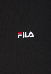 Svart tyg med ribbad textur som har en vit broderad "FILA"-logotyp och en röd accent i bokstaven 'F'.