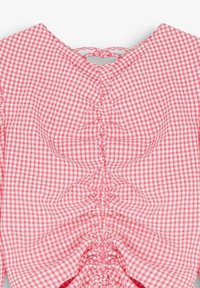 Blouse vichy rose et blanche avec fronces au centre et fermeture par lien au niveau de l'encolure arrière.